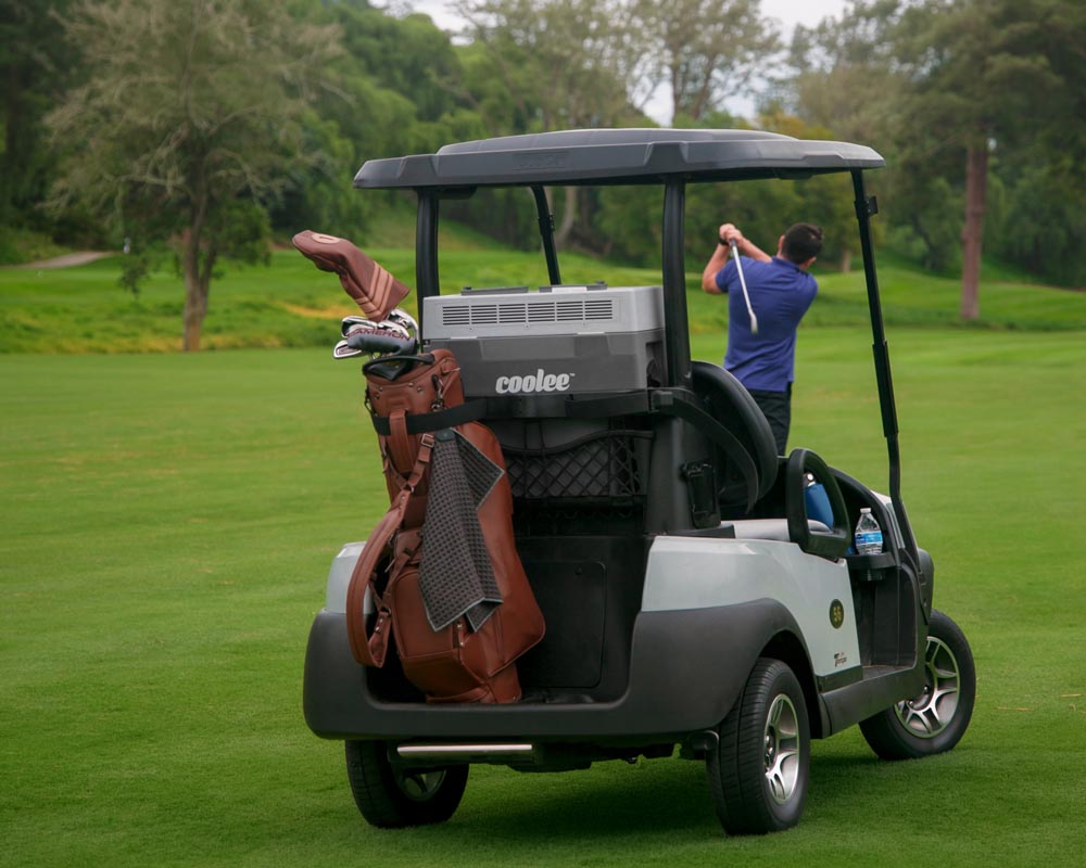 Coolee Tour LX portable air conditioner mounted in a golf cart rear basket while a golfer takes a swing.
