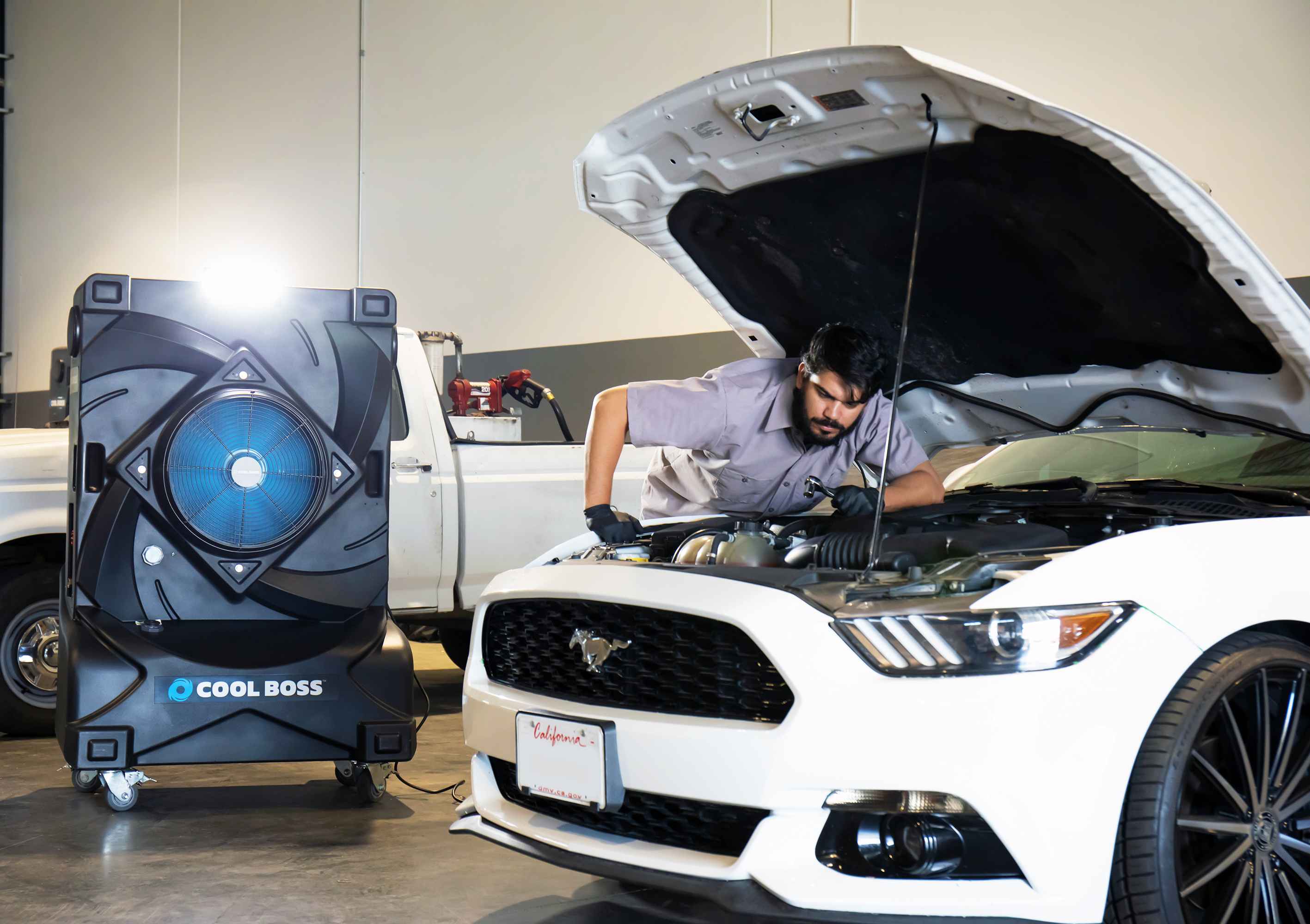 Technician working under the hood of a Ford Mustang in an auto shop with a Cool Boss evaporative cooler positioned beside the vehicle.